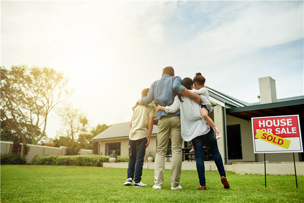 Family standing in front of their new home with a Sold sign in the yard